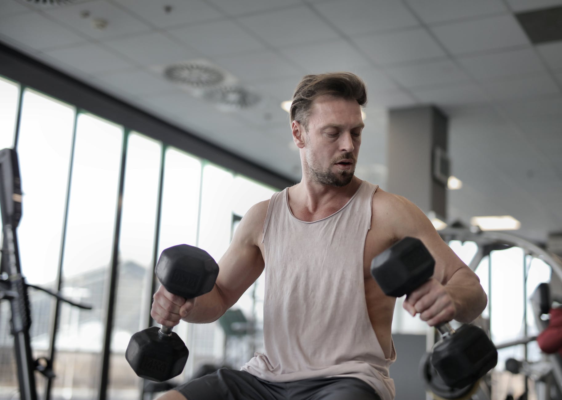 strong focused sportsman exercising with dumbbells in modern gym